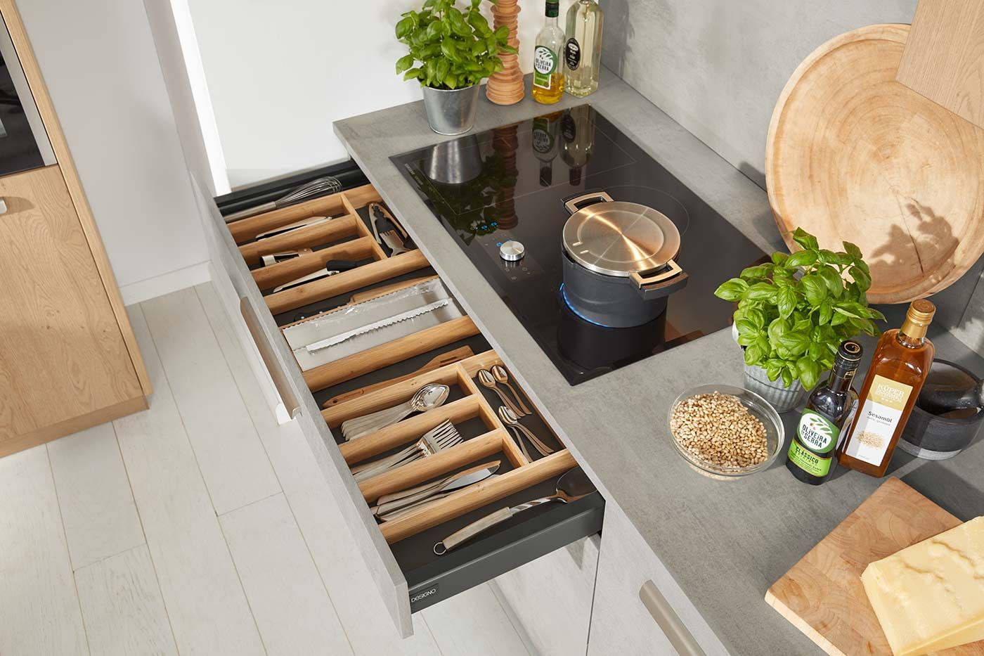 Geöffnete graue Küchenauszüge mit Einsätzen für Besteck und diverse Küchenutensilien.