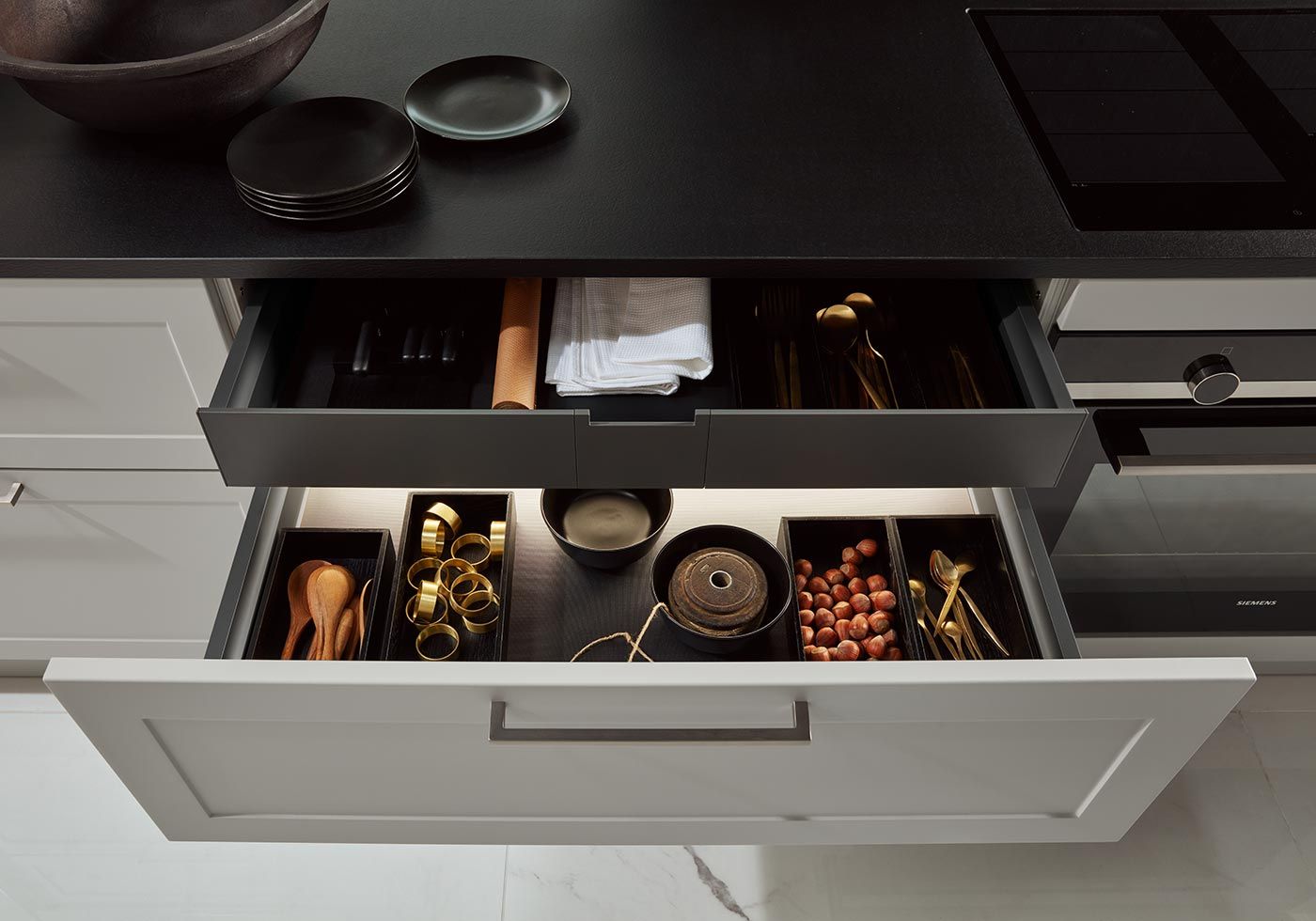 Geöffnete Schubladen mit Besteck, Serviettenringen und Nüssen in schwarzen Boxen.