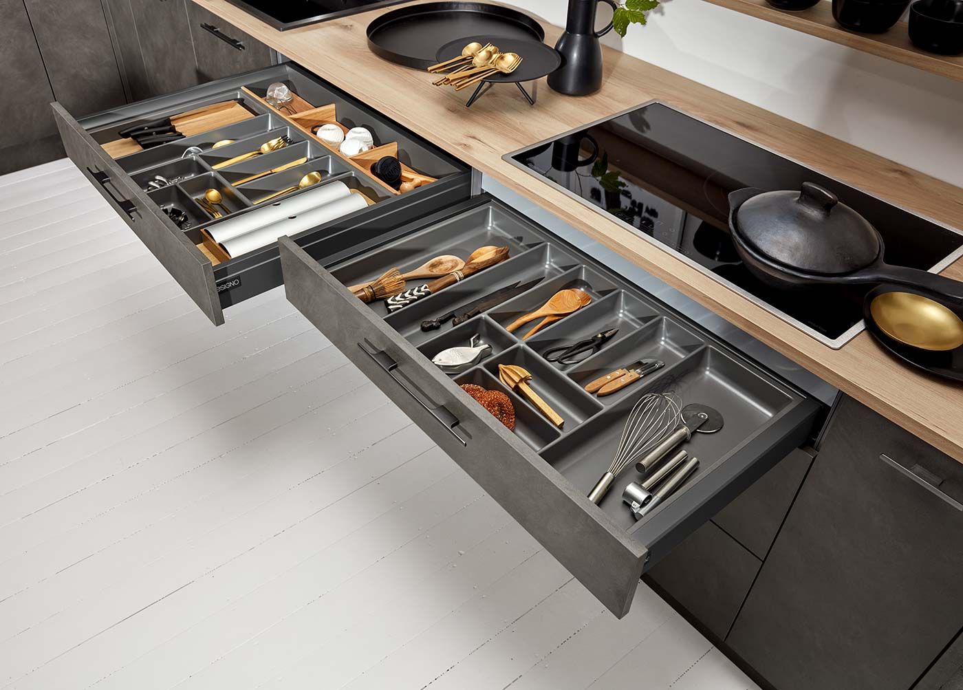 Zwei geöffnete graue Küchenschubladen mit strukturierten Einsätzen für Küchenhelfer.