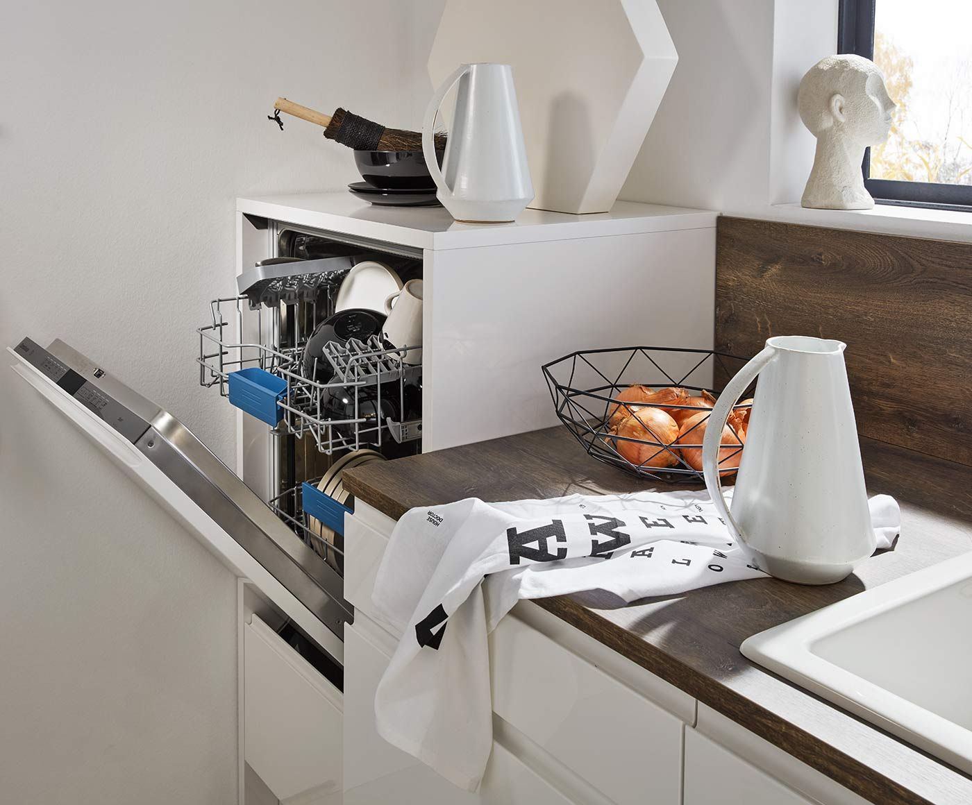 Geöffneter, hocheingebauter Geschirrspüler in weißer Küche mit dunkler Holz-Arbeitsplatte.