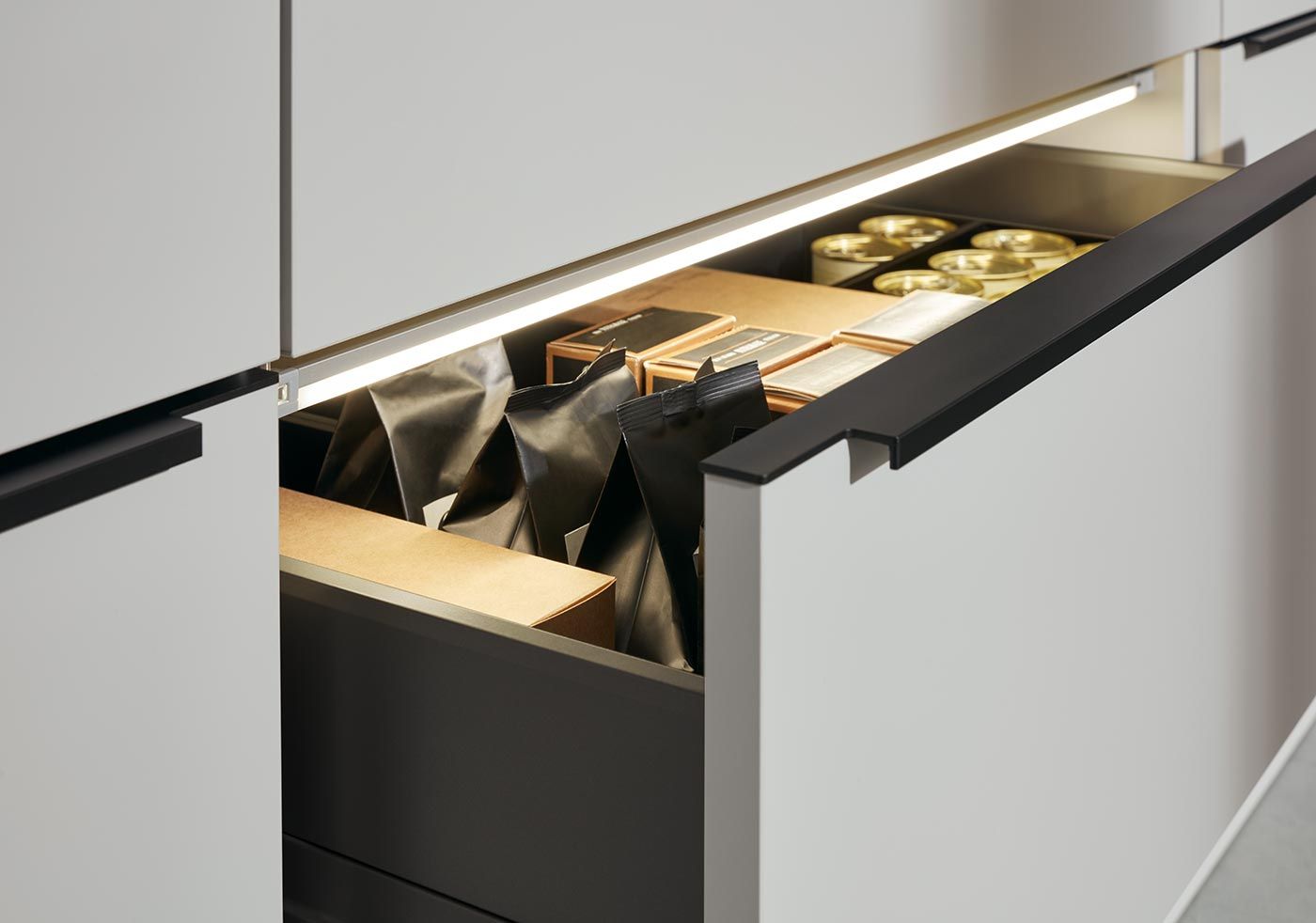 Geöffnete weiße Küchenschublade mit LED-Leiste, Vorratstüten und Konservendosen.