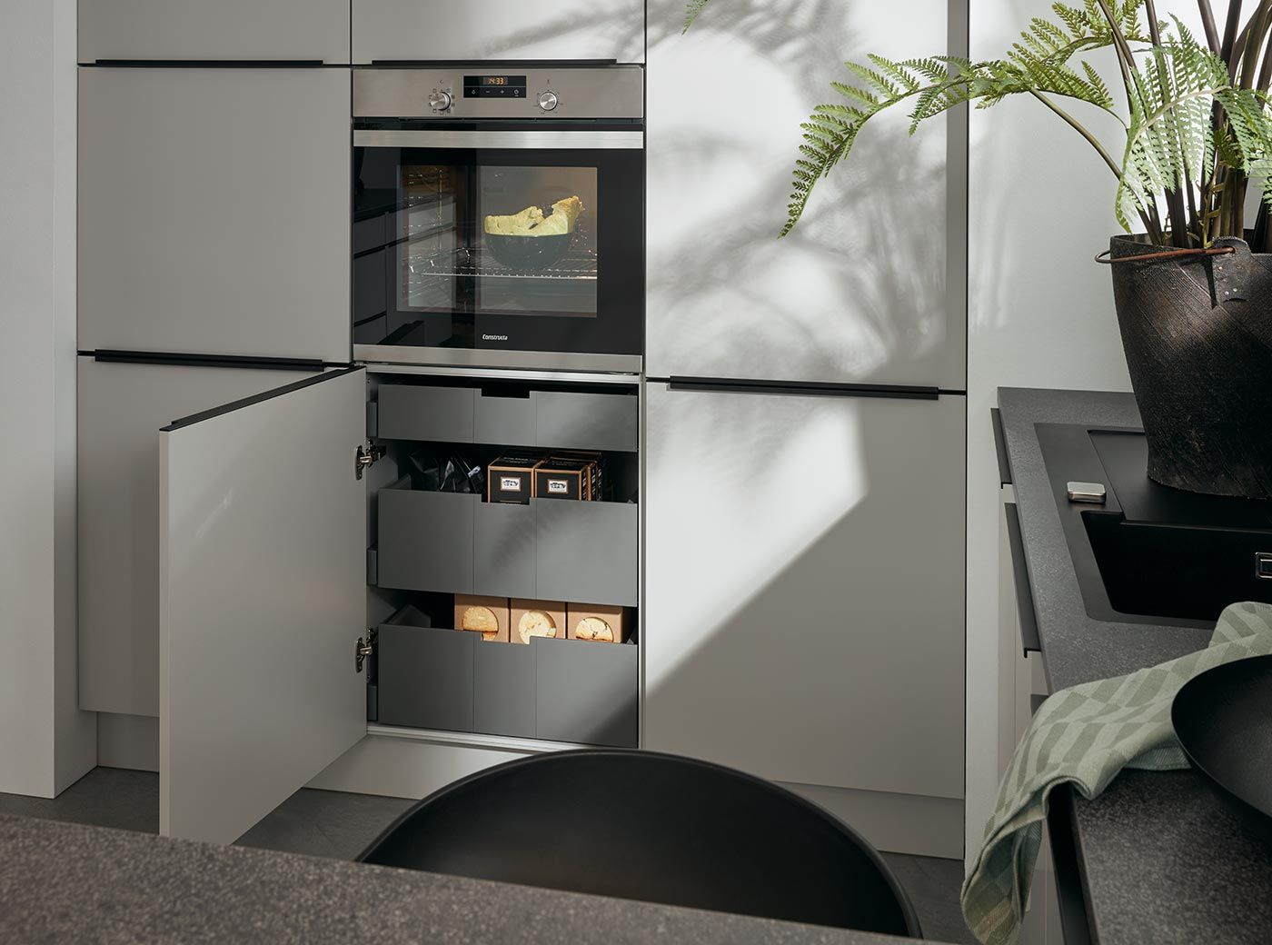 Grauer Unterschrank mit praktischen Innenauszügen unter einem modernen Einbaubackofen.