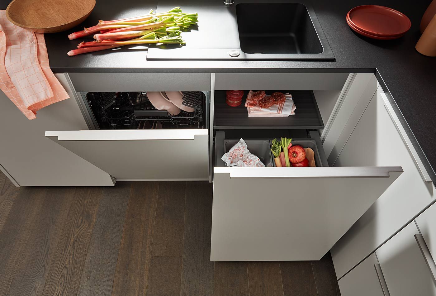 Ausziehbarer Abfalleimer und Geschirrspüler in weißer Eckküche mit Rhabarber.