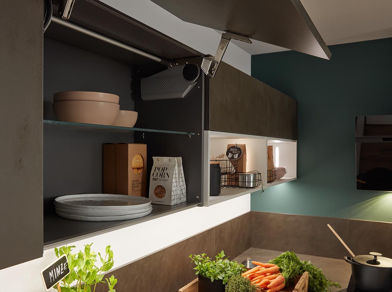 Geöffneter Lifttür-Oberschrank mit Glaseinlegeboden über beleuchteter Küchenarbeitsplatte.