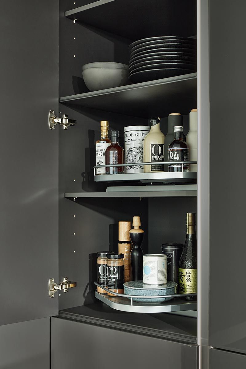 Geöffneter dunkler Küchenschrank mit ausziehbaren Tablaren für Flaschen und Gewürze.