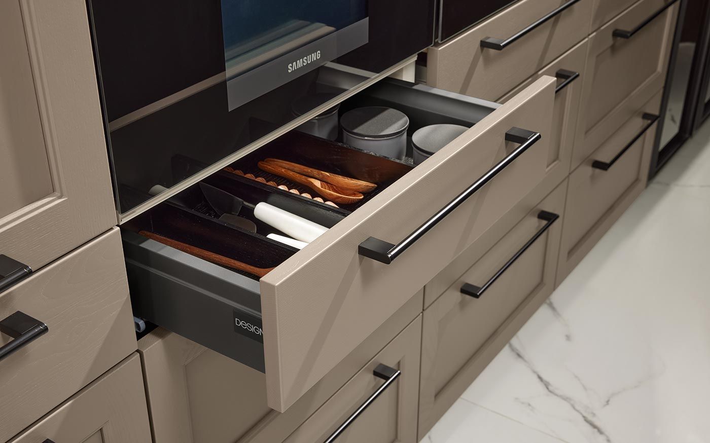 Geöffnete Schublade mit Holzeinsätzen für Besteck unter einem Samsung-Backofen.