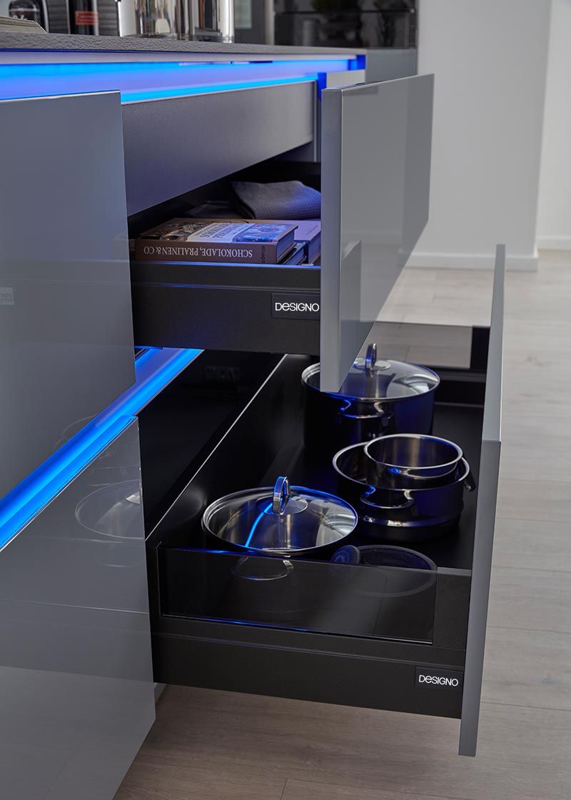 Graue Hochglanz-Schubladen mit blauer LED-Beleuchtung und verstauten Kochtöpfen.