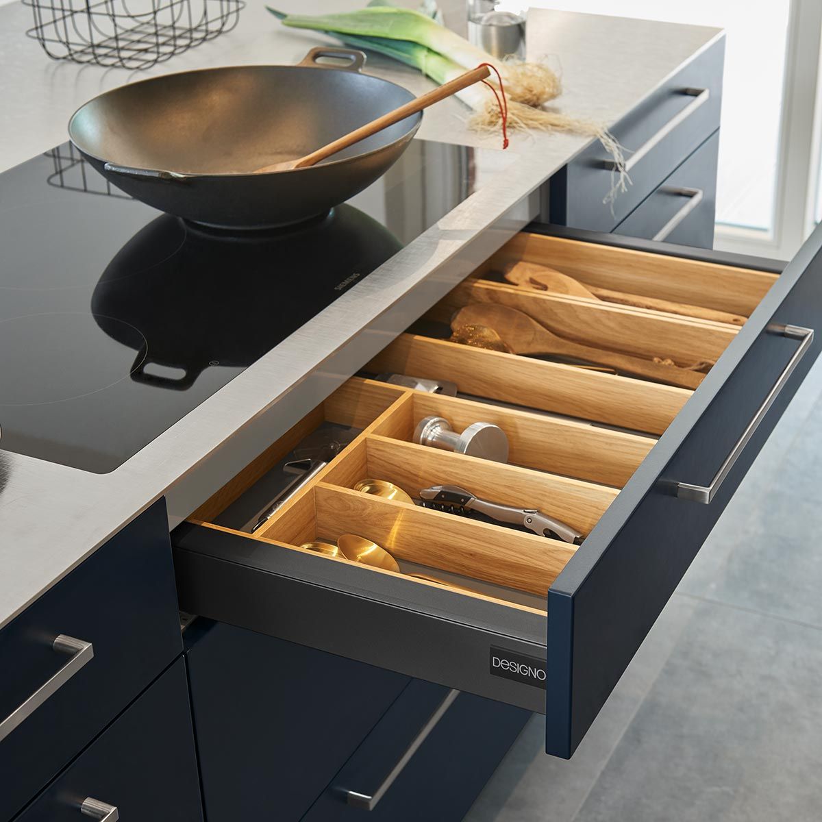 Geöffnete anthrazitfarbene Schublade mit hölzernem Besteck-Organizer neben einem Induktionskochfeld.