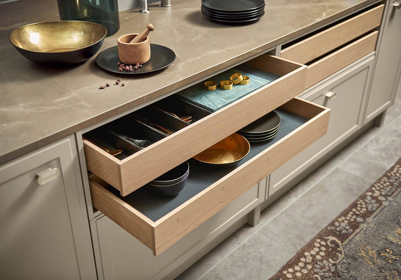 Geöffnete Holzschubladen mit Besteck und Schalen unter einer Steinarbeitsplatte.
