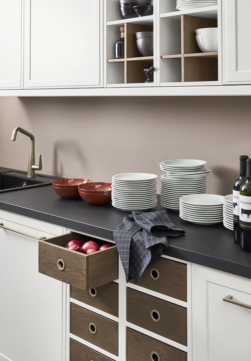 Weiße Küchenzeile mit dunkler Arbeitsplatte, Stapeln von Tellern und Holzschubfächern.