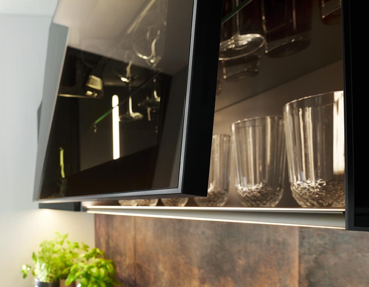 Geöffneter schwarzer Vitrinenschrank mit beleuchteten Glasböden und stilvollen Gläsern.