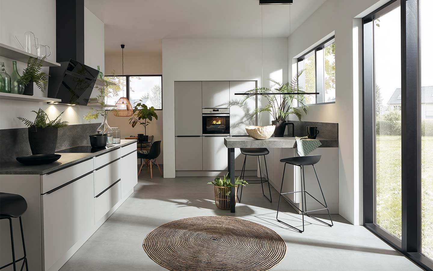 Moderne weiße Küche mit grauer Arbeitsplatte, Barhockern und viel Tageslicht.
