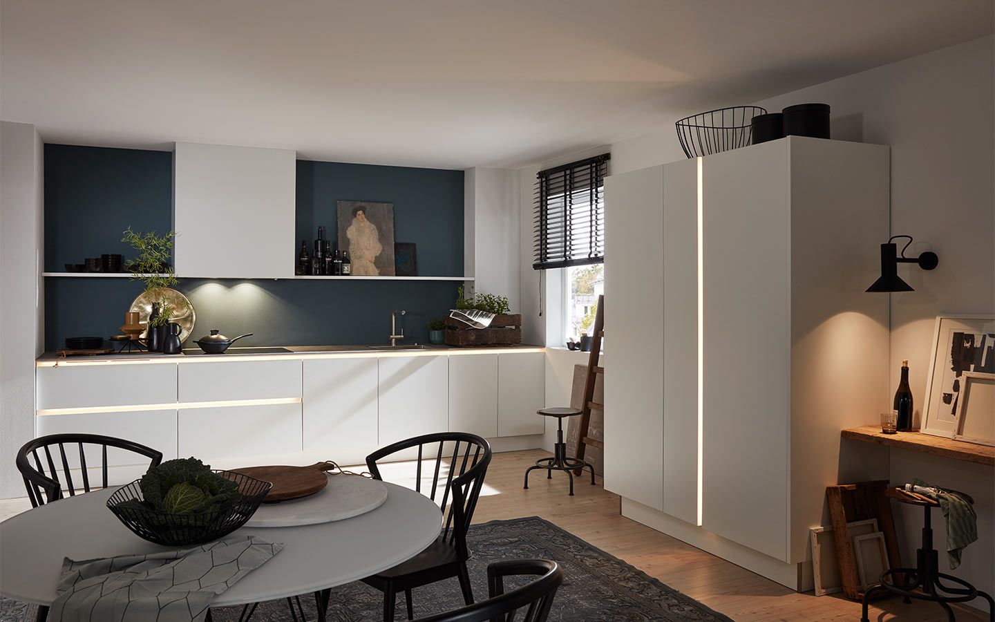Weiße Küchenzeile vor dunkelblauer Wand mit stimmungsvoller LED-Beleuchtung.