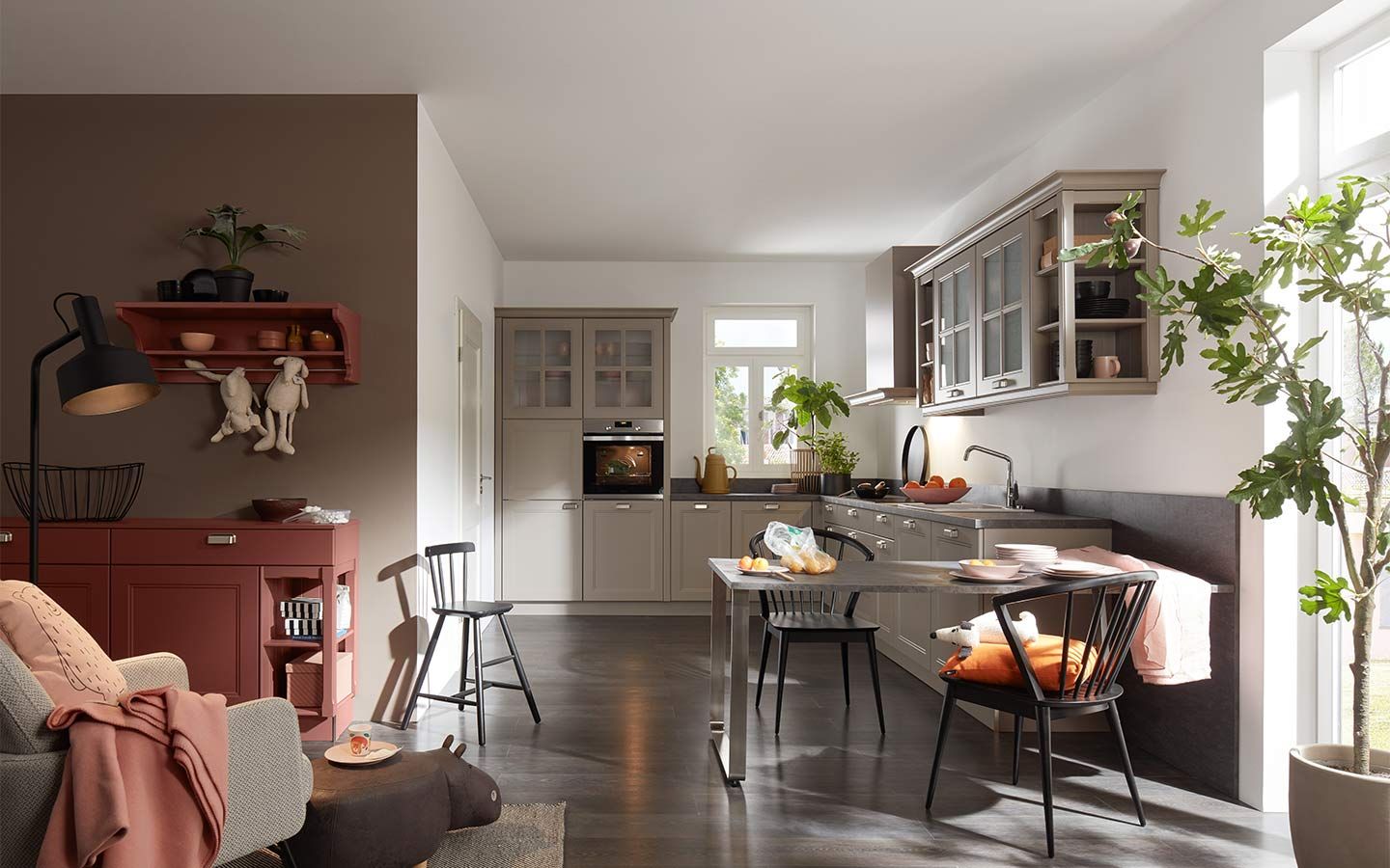 Beige Landhausküche mit Vitrinenschränken, Esstisch und terracottafarbenem Sideboard.