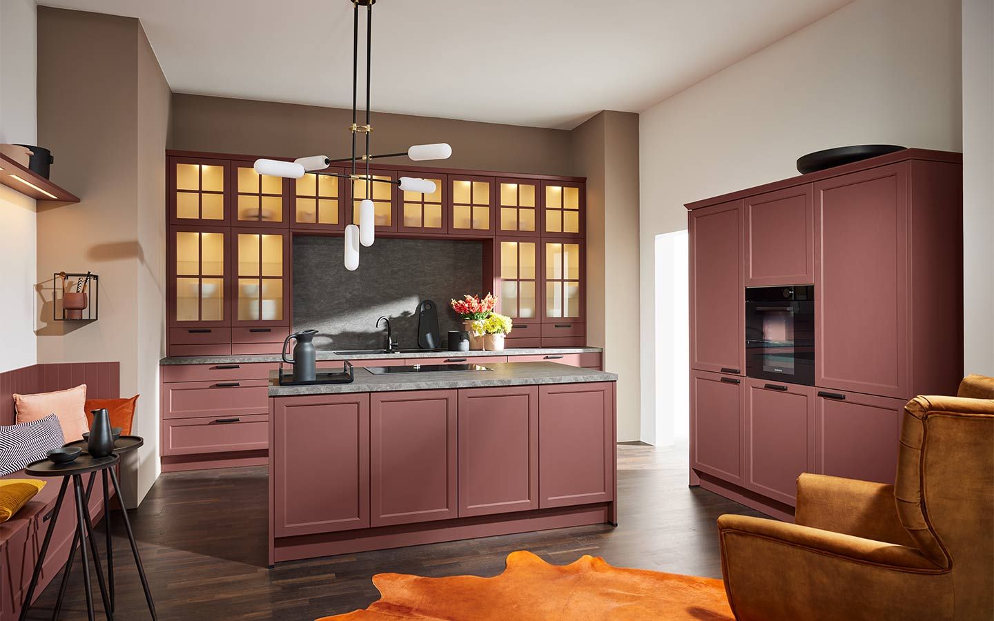 Bordeauxrote Küche mit Kochinsel, beleuchteten Vitrinen und moderner Kronleuchter-Beleuchtung.