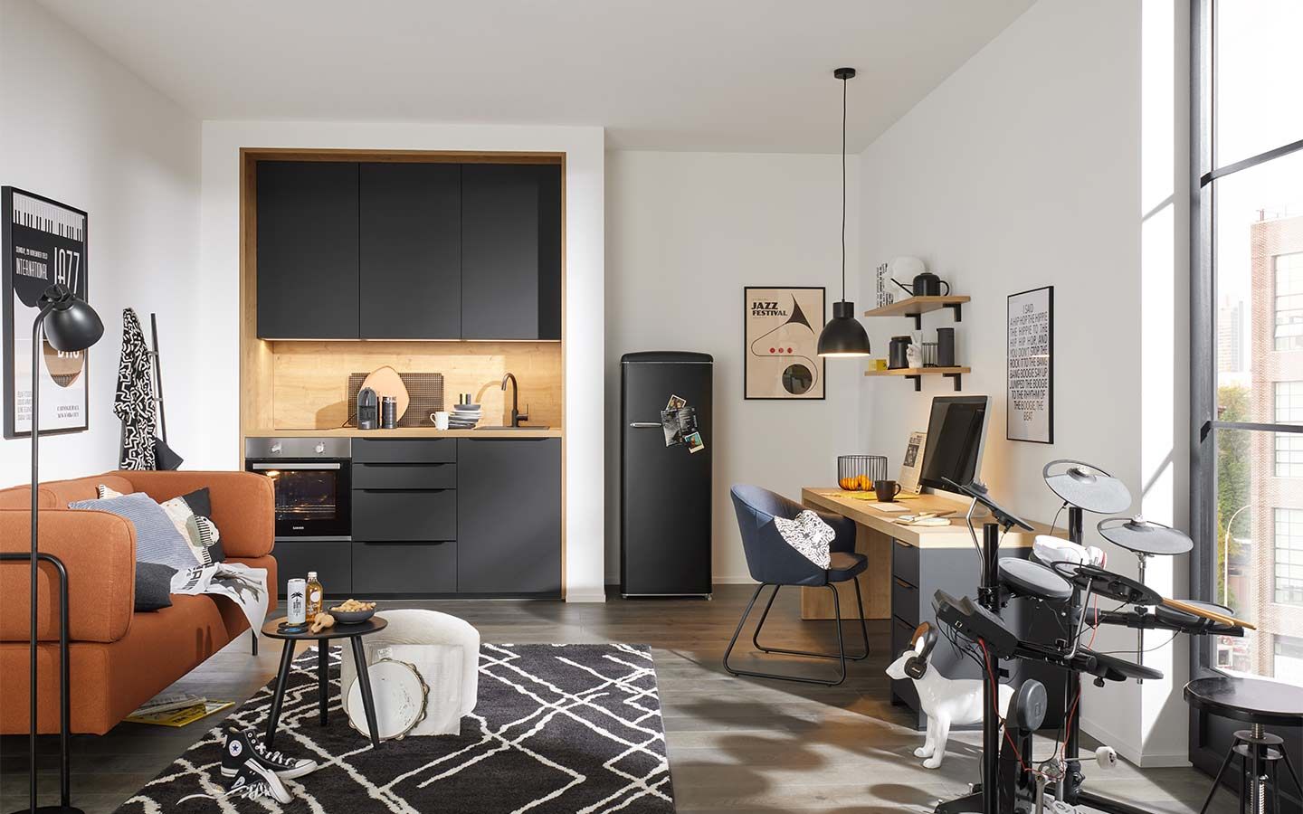 Modernes Studio mit schwarzer Küchenzeile, Arbeitsplatz und elektronischem Schlagzeug.