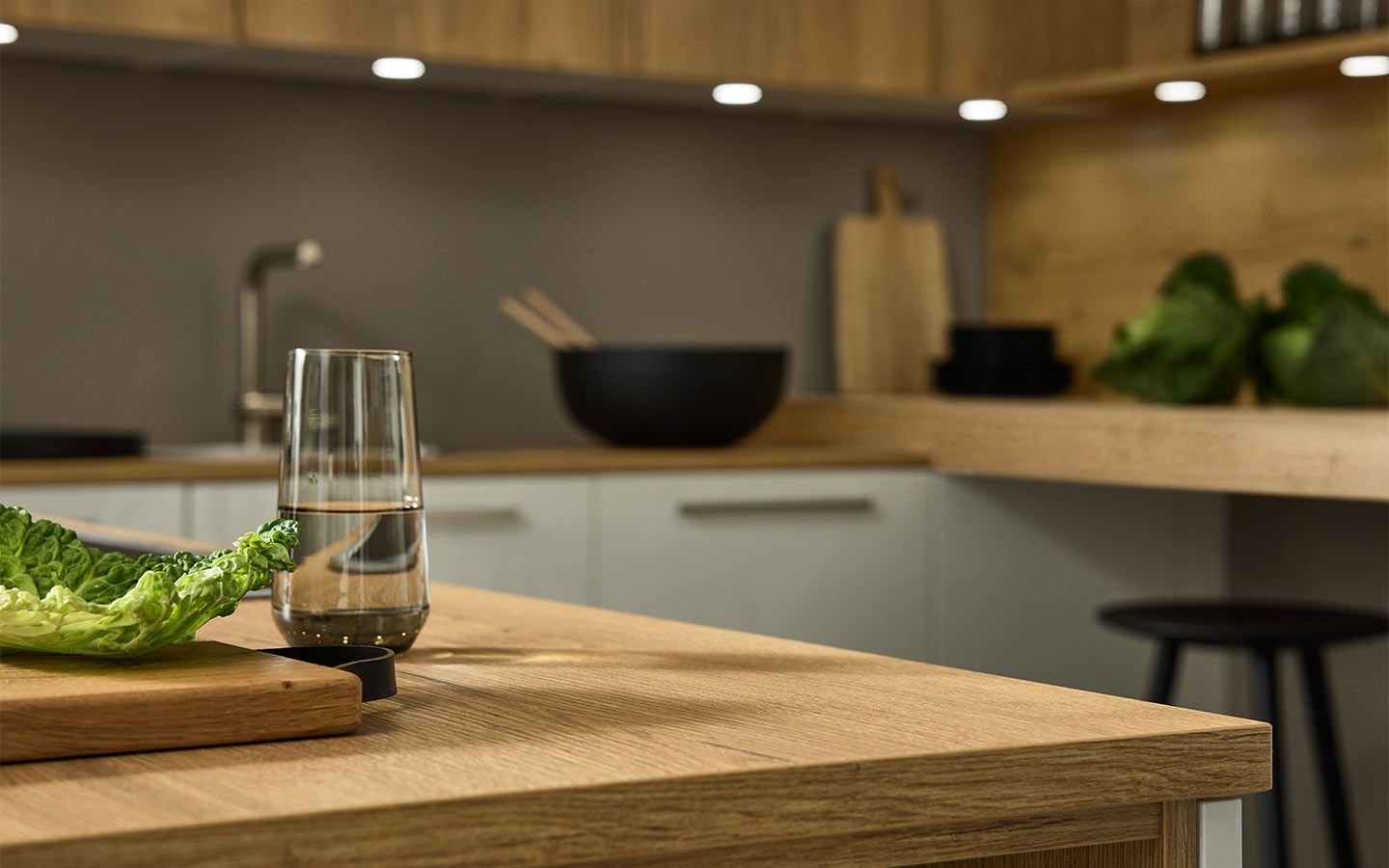 Fokus auf strukturierte Eichen-Arbeitsplatte mit Wasserglas und Salatblatt im Vordergrund.