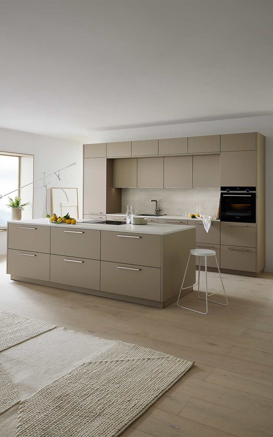 Minimalistische beige Küche mit großer Kochinsel und hellem Holzboden.