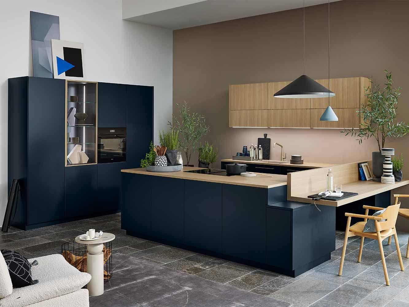 Marineblaue Küche mit Holz-Arbeitsplatte, Kochinsel und angebautem Schreibtisch-Element.