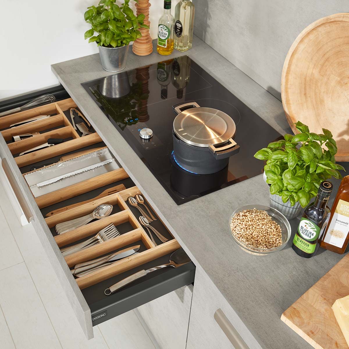 Topf auf dunklem Kochfeld und einer geöffneten Besteckschublade 